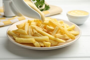 Pouring delicious cheese sauce onto French fries at wooden table, closeup