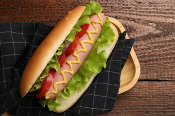 Tasty hot dog with tomato, onion, lettuce and mustard on wooden table, top view