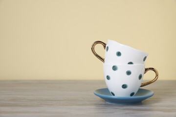 Beautiful cups and saucer on light wooden table against beige background. Space for text
