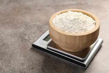 Digital kitchen scale with bowl of flour on grey textured table, closeup