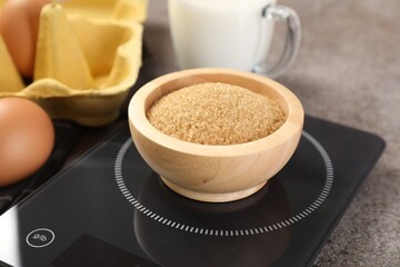 Digital kitchen scale with bowl of brown sugar and other products on grey table, closeup