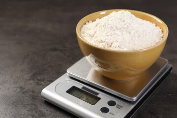 Digital kitchen scale with bowl of flour on grey table, closeup. Space for text