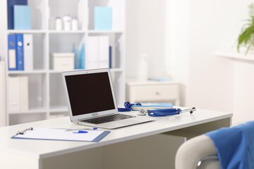 Doctor's workplace with stethoscope, paperwork and laptop on desk