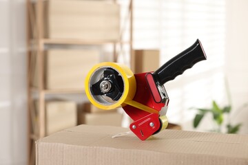 Dispenser with adhesive tape on cardboard box indoors, closeup