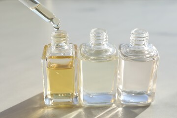 Taking aromatic oil from perfume bottle with dropper on light background, closeup
