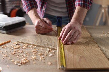 Man measuring wooden plank with tape indoors, closeup
