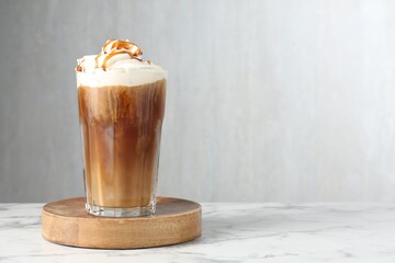 Tasty iced coffee with whipped cream and syrup on white marble table. Space for text