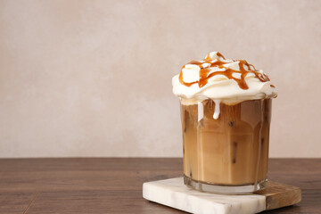 Tasty iced coffee with whipped cream and syrup on wooden table. Space for text