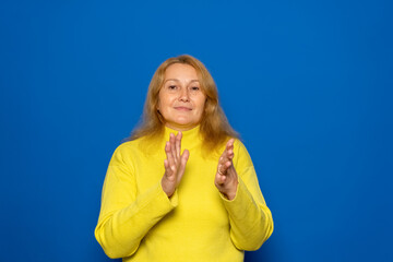 Caucasian woman in her 40s feeling happy and successful, smiling and clapping, saying congratulations with a handclap against a blue wall.