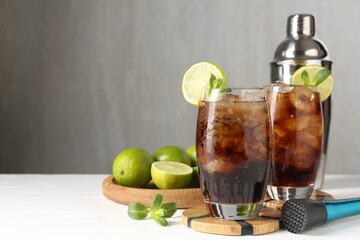 Tasty Cuba Libre cocktail in glasses, ingredients, muddler and shaker on white wooden table, space for text