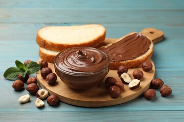 Chocolate hazelnut spread in bowl, nuts and toasts on light blue wooden table, closeup