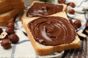 Toasts with chocolate hazelnut spread and nuts on wooden table, closeup