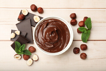 Chocolate hazelnut spread in bowl, nuts, pieces of chocolate and mint on wooden table, flat lay