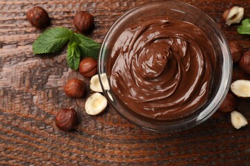 Chocolate hazelnut spread in bowl, nuts and mint on wooden table, flat lay