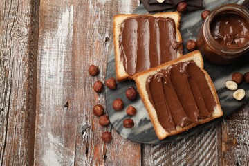 Toasts with tasty chocolate hazelnut spread and nuts on wooden table, flat lay. Space for text