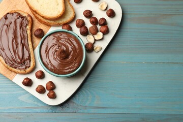 Toast with tasty chocolate hazelnut spread and nuts on blue wooden table, top view. Space for text