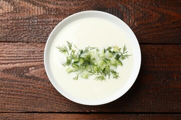 Tasty cucumber soup in bowl on wooden table, top view