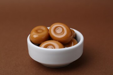 Tasty sweet caramel candies on brown background, closeup