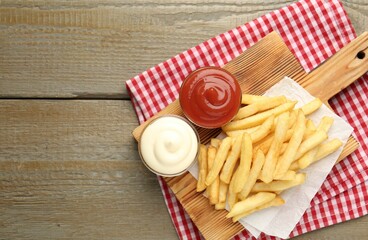 Tasty french fries with sauces on wooden table, top view. Space for text