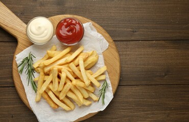 Tasty french fries with sauces and rosemary on wooden table, top view. Space for text