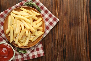 Tasty french fries served with ketchup and rosemary on wooden table, top view. Space for text