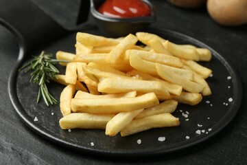 Tasty french fries served with ketchup and rosemary on black table, closeup