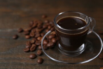 Aromatic coffee in glass cup and beans on wooden table, closeup. Space for text
