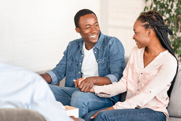 Happy african american couple visiting social worker before adoption, smiling black spouses sitting on couch, preparing child custody, sitting on consultation with family counselor, free space