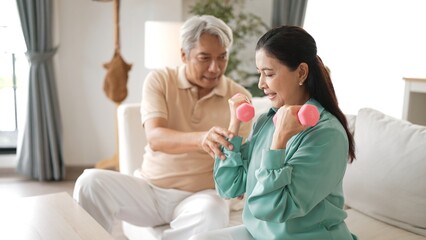 Happy elderly couple exercising together with dumbbells at home, focusing on muscle strength, joint health, and physical wellness for improved mobility and healthy aging. Retirement concept. Myrmidon.