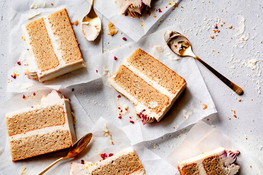 Slices of layered cake with frosting on parchment paper, accompanied by gold spoons.