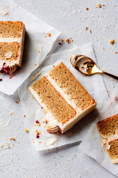 Three slices of layered cake with cream frosting are placed on parchment paper, accompanied by a golden spoon and crumbs scattered on a textured surface.