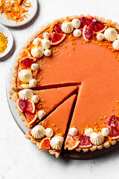 An orange tart garnished with whipped cream and slices of blood orange, displayed on a plate with decorative elements around it.