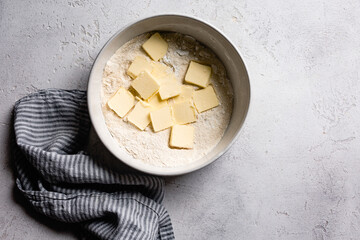 A bowl with flour and butter slices on a textured surface beside a striped cloth.