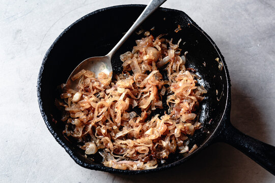 A cast iron skillet filled with caramelized onions, glistening and golden brown, with a spoon resting inside.