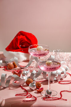 festive New Year table setting, two pink cocktails garnished with lychee and appetizers, red beads, silver ribbons, sparkly ornaments, for Christmas parties
