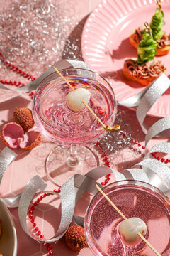 festive New Year table setting, two pink cocktails garnished with lychee and appetizers, red beads, silver ribbons, sparkly ornaments, for Christmas parties