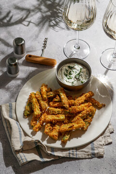 Healthy crunchy zucchini nuggets with sauce, on a grey stone background with bright sunlight, and a glass of white wine