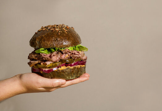 gourmet Roast Beef Sandwich, fresh lettuce, pickles, red onion, held person's hands, with a neutral background and hash sun lighting