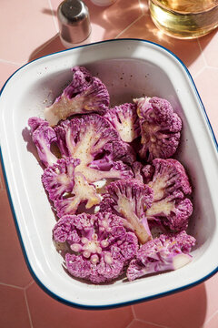purple cauliflower with bechamel sauce in a baking dish, on a pink ceramic tile, hard light