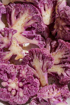 purple cauliflower with bechamel sauce in a baking dish, on a pink ceramic tile, hard light