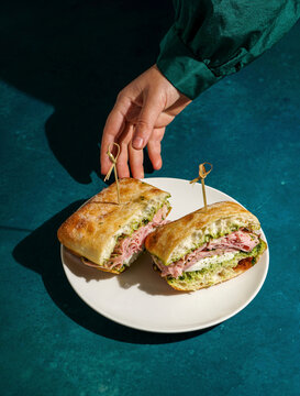 delicious  Italian Mortadella Sandwich with Pesto and Mozzarella basil pesto, crusty ciabatta bread, in the hands, against a deep green fabric background