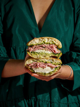 delicious  Italian Mortadella Sandwich with Pesto and Mozzarella basil pesto, crusty ciabatta bread, in the hands, against a deep green fabric background