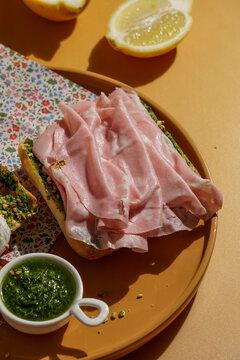 delicious  Italian Mortadella Sandwich with Pesto and Mozzarella basil pesto, crusty ciabatta bread, yellow background