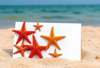 Several starfish arranged on a blank white card resting on sandy beach, starfish on beach, sea