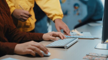 A closeup view of hands at a computer in a vibrant office setting, showcasing professionals...