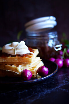 Australian Lilly Pilly Riberry Jam against a black background, served with waffles and cream.