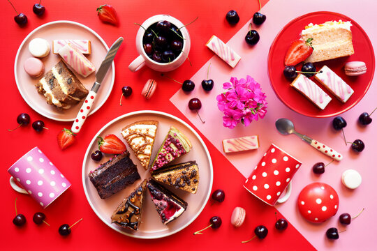 Pop art food, color blocking aesthetic with double layer cream filled assorted cakes, cherries, macarons and strawberries.
