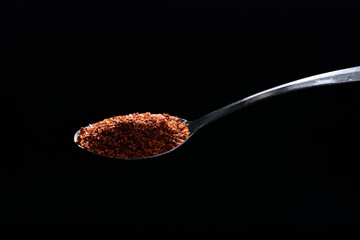 Close up cayenne spices on spoon isolated on black background.