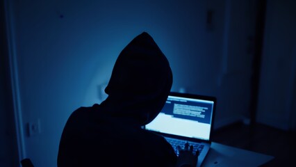 Hacker hacks programs. Computer scammer. Programmers working intently on laptop, typing in dark room with shadowy atmosphere, evoking cybersecurity intensity and digital intrigue