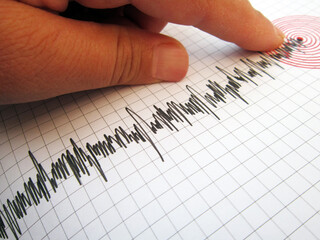     Seismograph and earthquake. A hand pointing at a seismograph recording the seismic activity of an earthquake                           